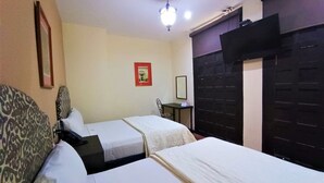 Habitació d'hotel amb dos llits, una taula petita, una cadira i una làmpada al sostre.