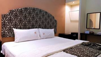 Quarto de hotel com uma cama grande, cabeceira estampada, mesa de cabeceira com abajur e um espelho na parede.