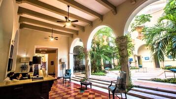 Um hall com piso xadrez, tetos em arco e uma mesa de recepção com cadeiras.