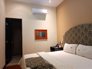 A hotel room with a bed, a nightstand, a framed picture, and an air conditioning unit. - Experience Mérida Your Way | Comfortable Stay + Pool (Mérida)