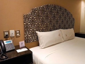 A hotel room with a patterned headboard, a desk with a telephone, and a sign indicating no smoking. - Experience Mérida Your Way | Comfortable Stay + Pool (Mérida)