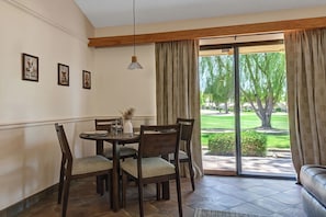A dining area with a round table, chairs, and a view of a green landscape through a glass door. - Relaxing 2 Bedroom Palm Resort Escape (Palm Desert)