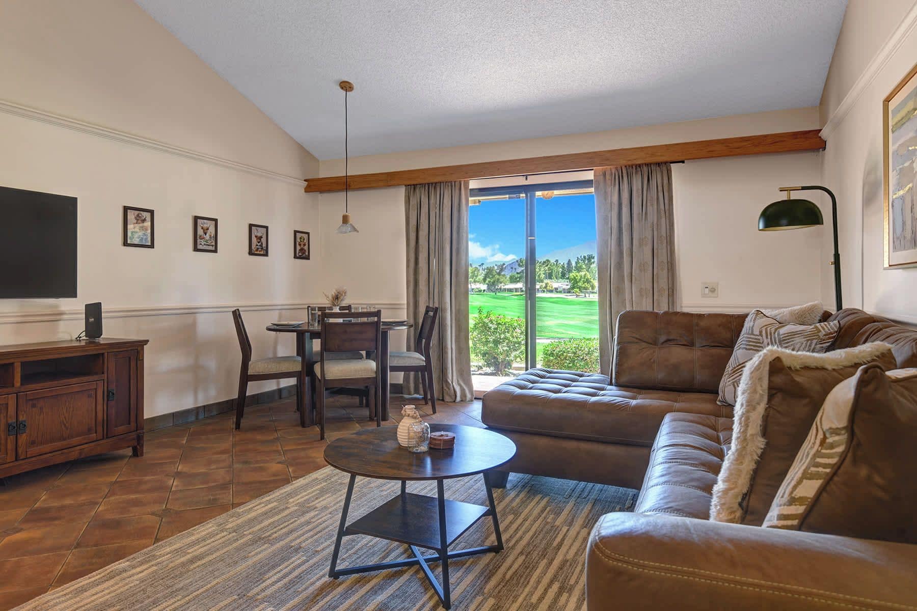 A living room with a sofa, a coffee table, a TV, and a dining area with chairs and a table.
