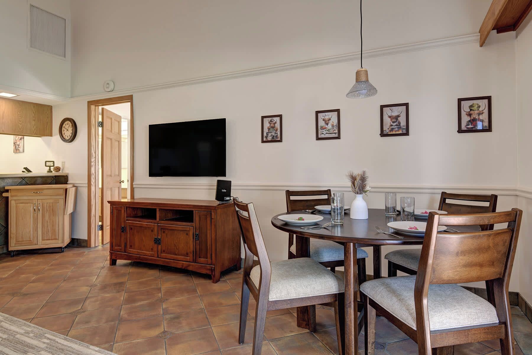 A dining area with a wooden table, chairs, and a television mounted on the wall.