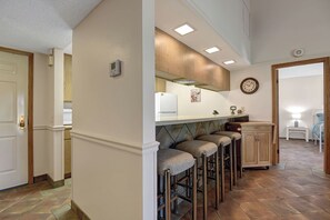 A kitchen with a white refrigerator, a clock, and a bar stool area. - Relaxing 2 Bedroom Palm Resort Escape (Palm Desert)
