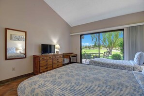 A hotel room with two beds, a desk, a TV, and a large sliding glass door leading to a patio with a view of a golf course. - Relaxing 2 Bedroom Palm Resort Escape (Palm Desert)