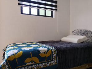 A bedroom with a bed, a window with blinds, a pillow, and a blanket.