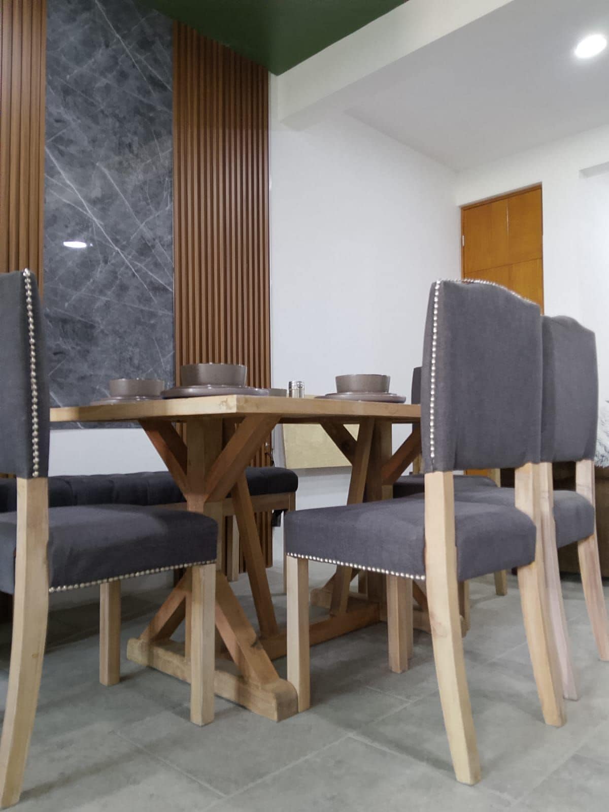 Un comedor con una mesa y sillas de madera, una pared de mármol y un panel de madera.