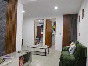 Una sala moderna con un sofá verde, una mesa de centro y un comedor con una mesa y sillas.