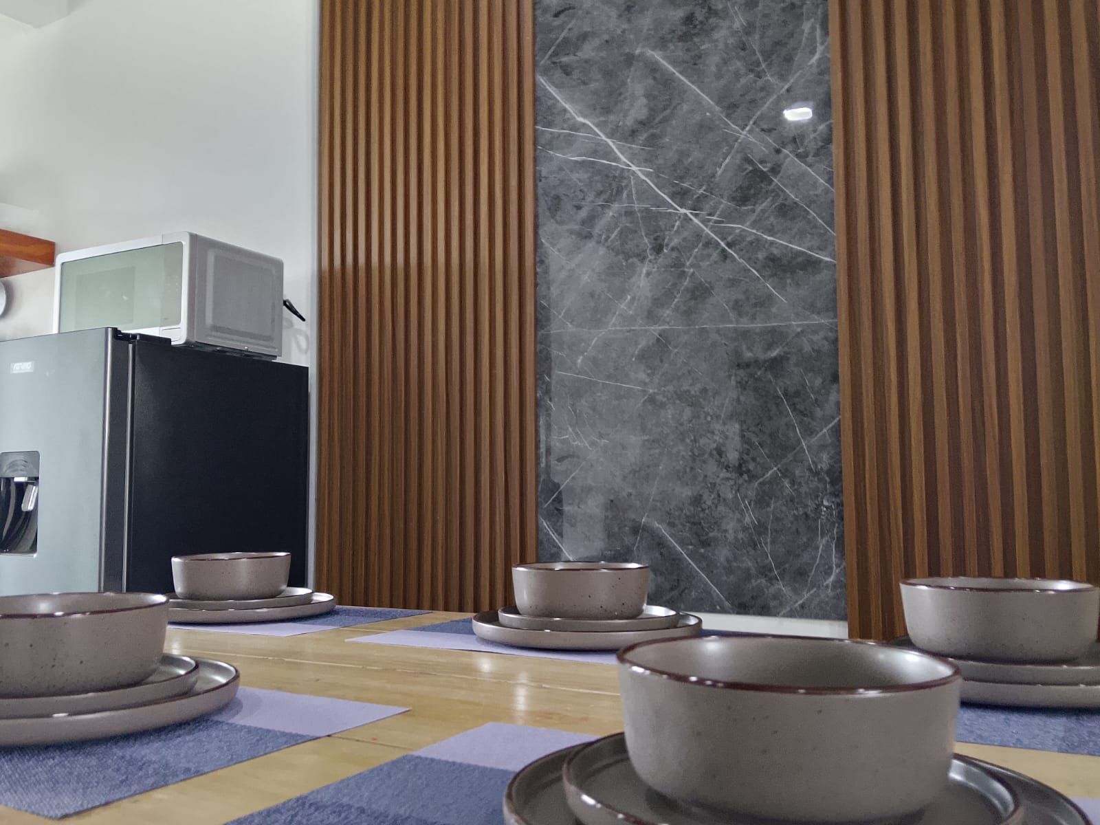 A kitchen with a refrigerator, microwave, and a marble backsplash.