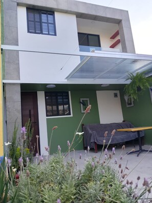 A modern two-story building with a flat roof, large windows, and a covered outdoor seating area.