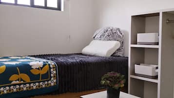 Une chambre à coucher avec un lit, une table de chevet ornée d’une plante, une fenêtre avec des stores et une armoire.