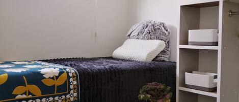 Une chambre à coucher avec un lit, une table de chevet ornée d’une plante, une fenêtre avec des stores et une armoire.