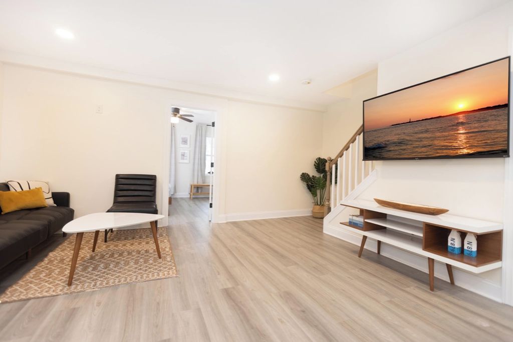 A modern living room with a flat-screen TV mounted on the wall, a sofa, a coffee table, and a staircase leading to another room.