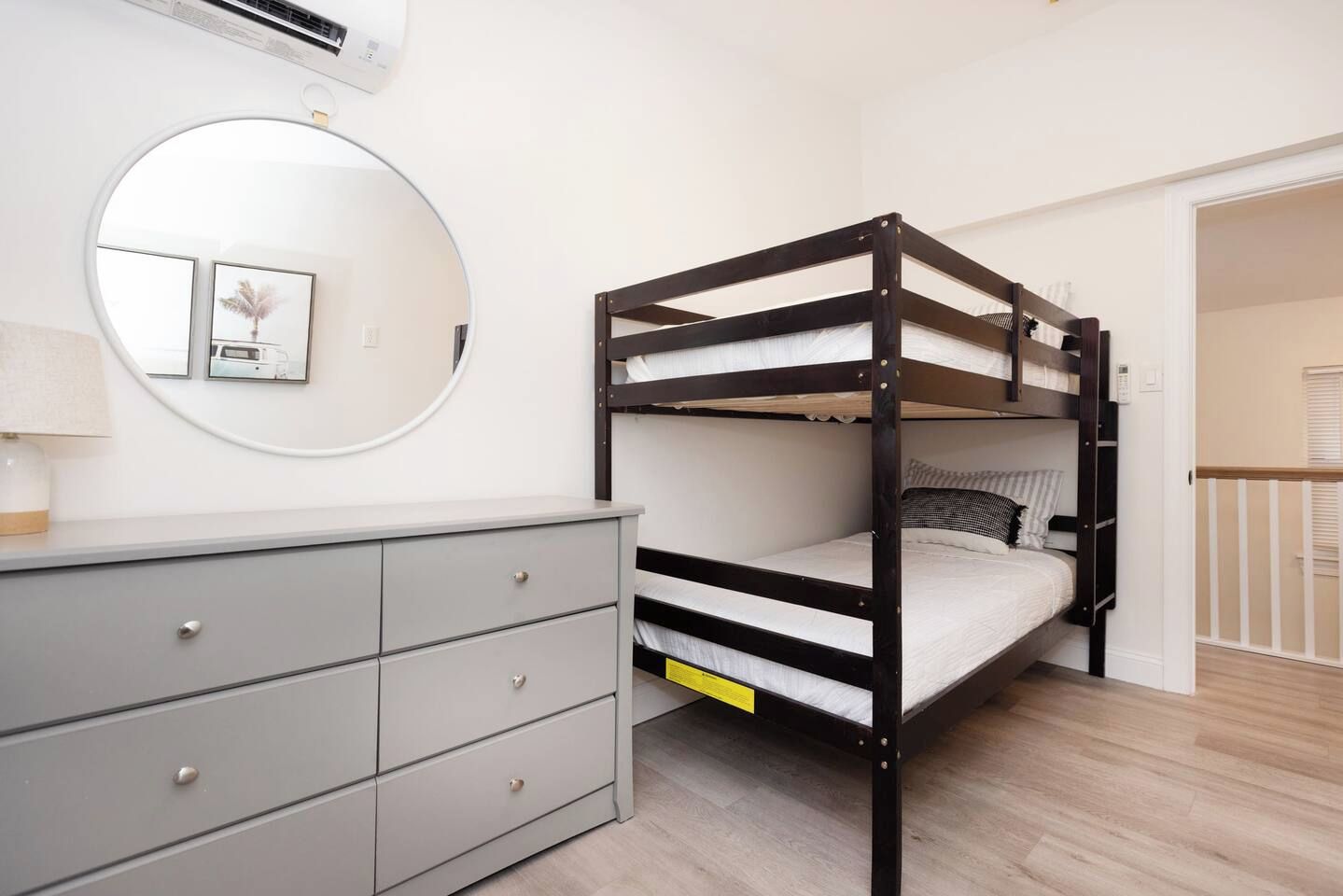 Una cama litera con un aparador gris y un espejo redondo en la pared.