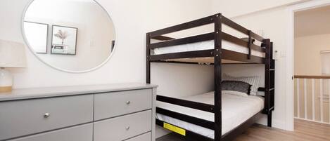 A bunk bed with a grey dresser and a round mirror on the wall.