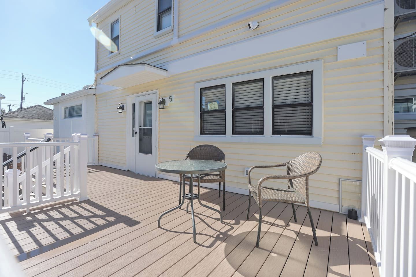 A wooden deck with a glass table and two wicker chairs.
