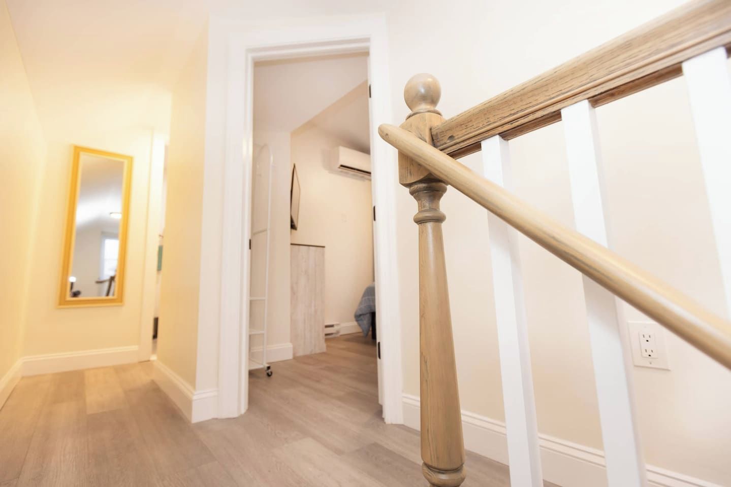 Un pasillo con una escalera de madera, un espejo y una puerta que da a otra habitación.