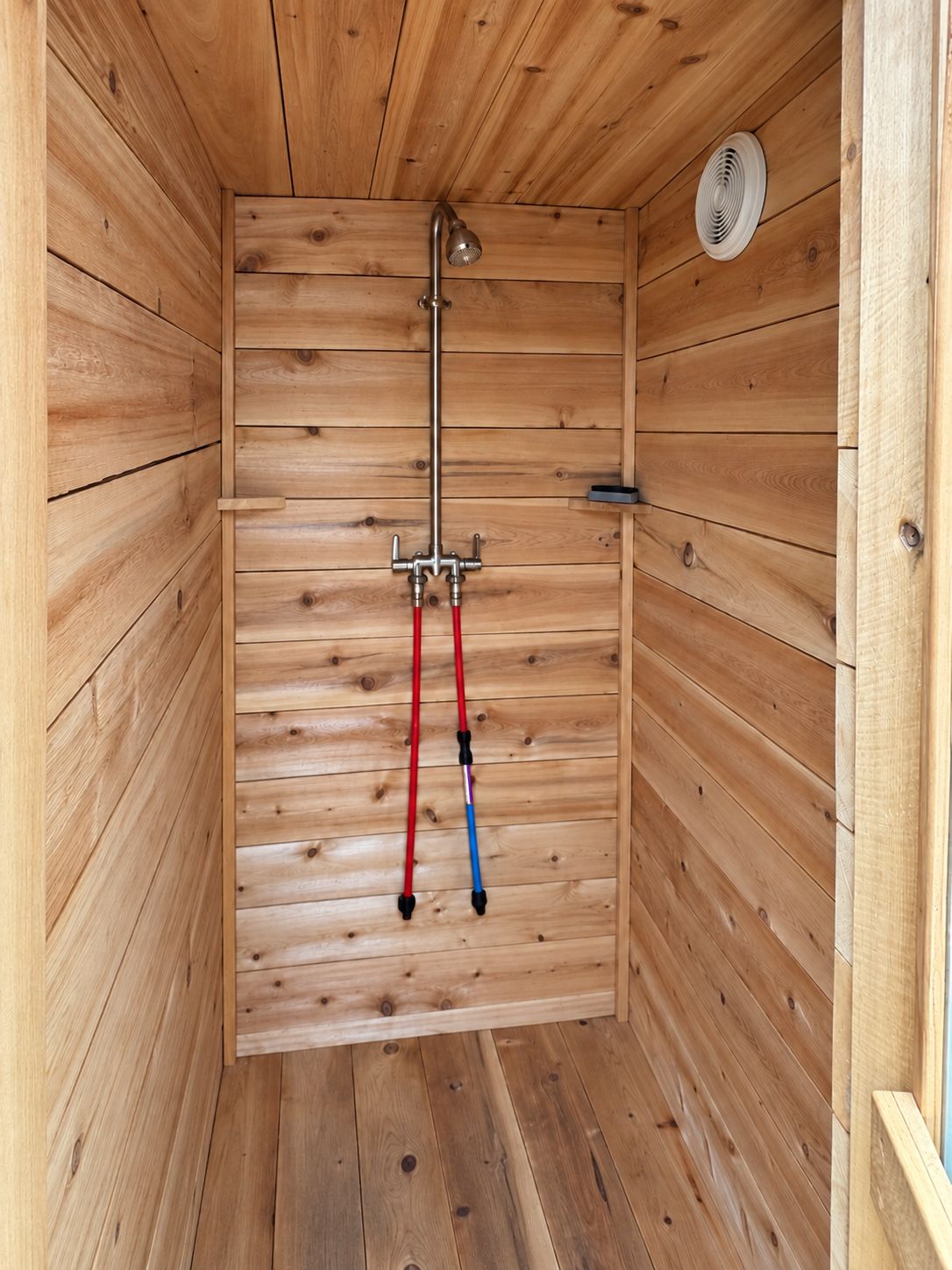 Una cabaña de madera con zona de ducha, que incluye un cabezal de ducha y mangueras.