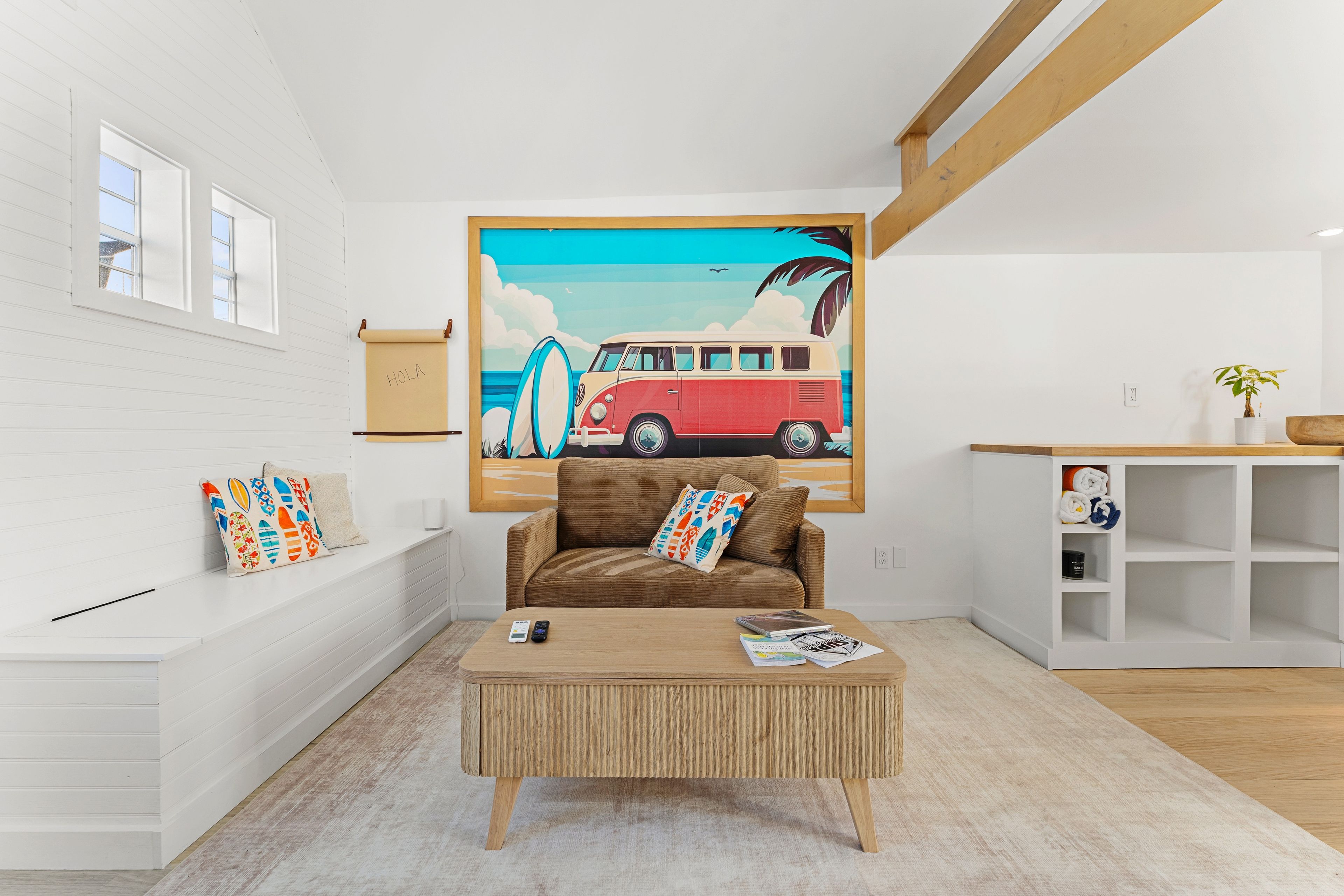 A modern living room with a brown sofa, a wooden coffee table, and a large beach-themed painting on the wall.