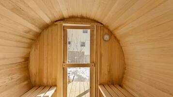 A sauna with wooden walls and benches, a door with a view of the outside, and a wall-mounted thermometer.