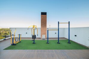 An outdoor gym with exercise equipment, a brick wall, and a clear sky. - Zuba IV Studio | Rooftop Pool & WiFi (Luque)