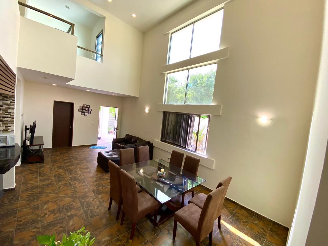 A spacious dining area with a glass table and chairs, a kitchen with a microwave, and a view of greenery outside.
