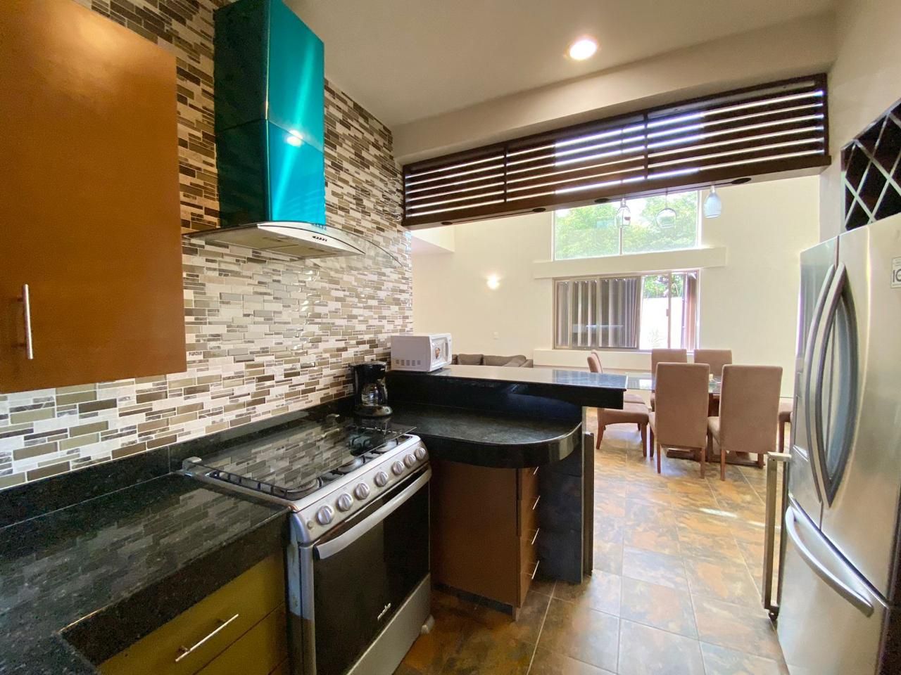 A modern kitchen with a gas stove, oven, and a refrigerator. There is a dining area with chairs and a table.