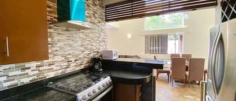 A modern kitchen with a gas stove, oven, and a refrigerator. There is a dining area with chairs and a table.