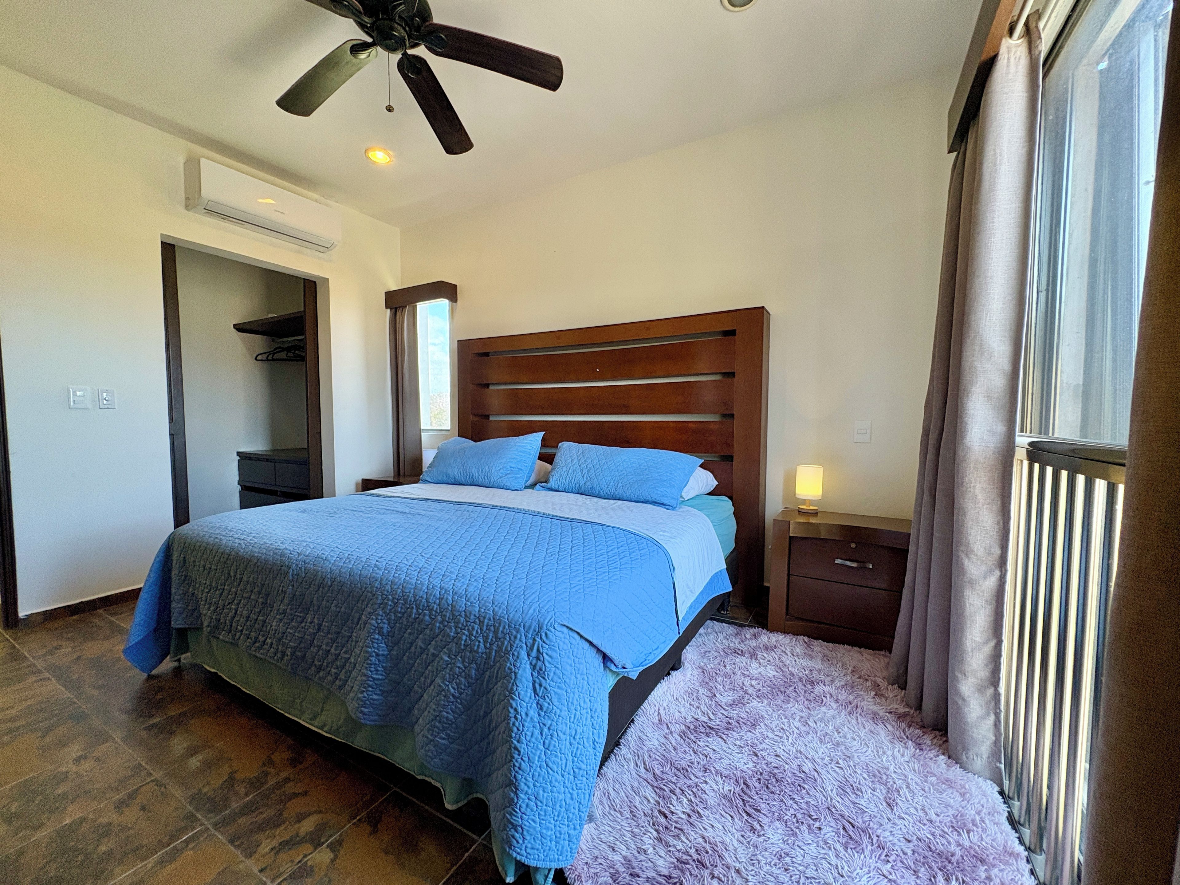A bedroom with a bed, a nightstand, a ceiling fan, and a window with curtains.