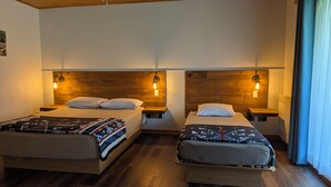 A hotel room with two beds, wooden headboards, bedside lamps, and a window with curtains. - L'Ours Bleu (Lac-Saguay)