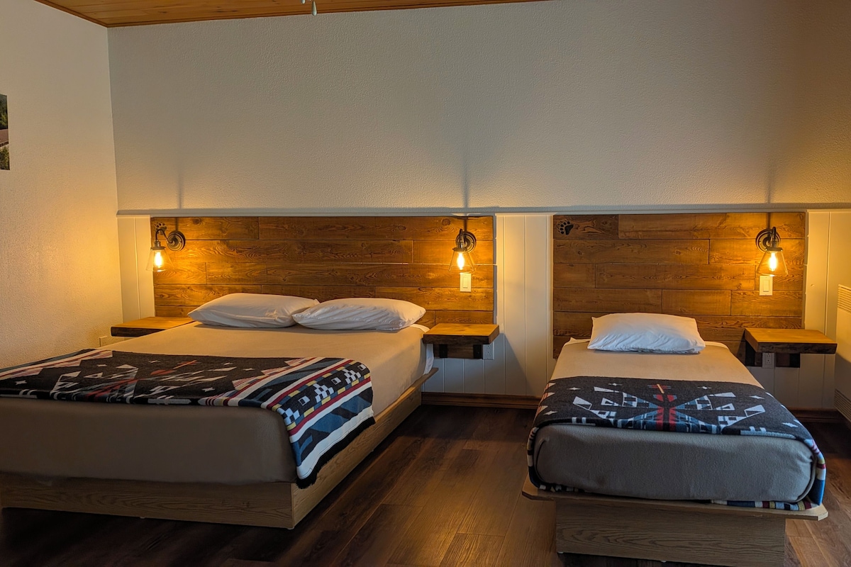 A hotel room with two beds, wooden headboards, bedside lamps, and a window with curtains.