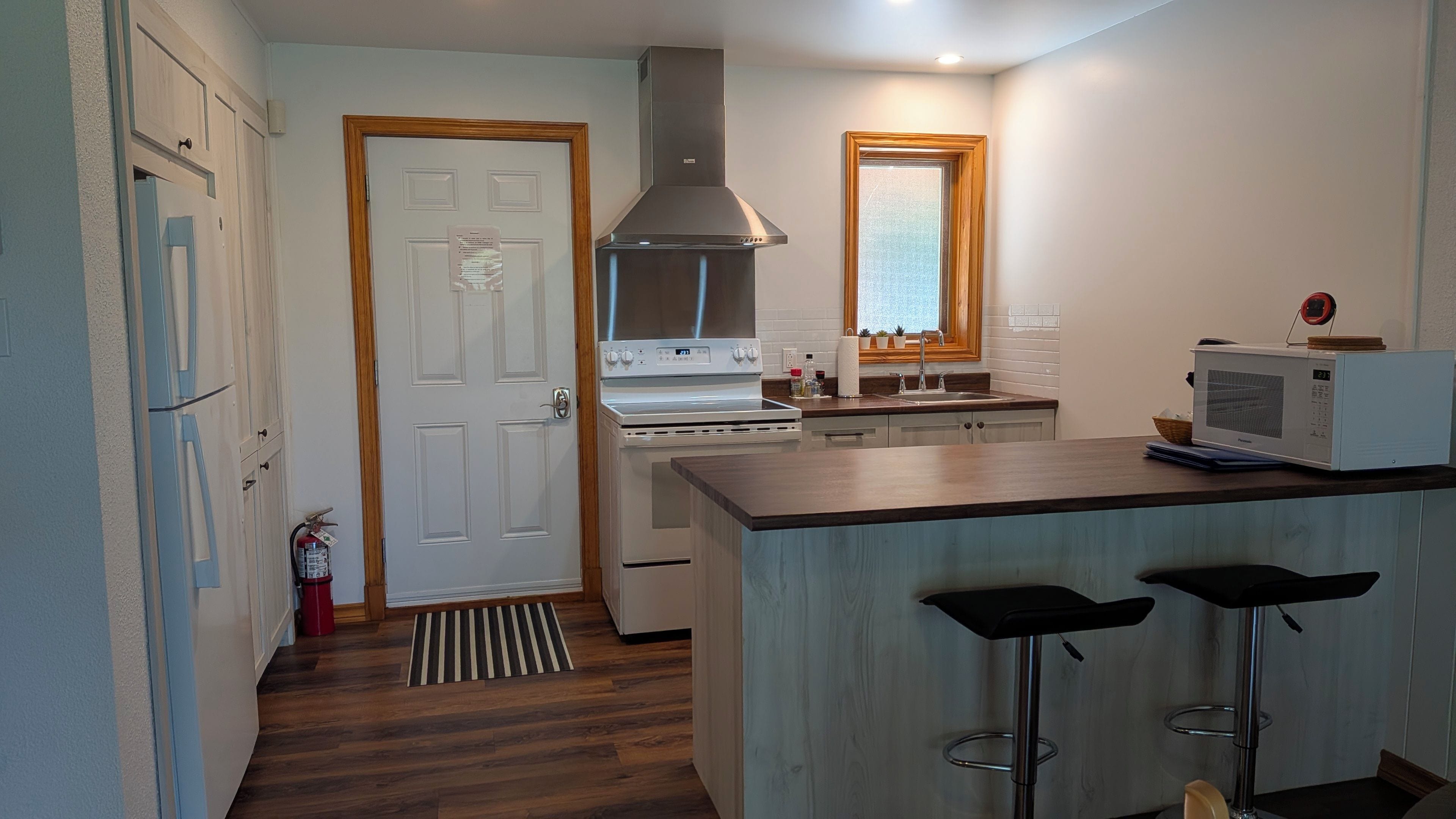 A modern kitchen with a stove, microwave, and bar stools.