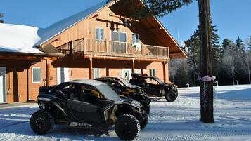Una cabaña de madera con balcón, dos cuatrimotos estacionadas adelante y terreno cubierto de nieve.