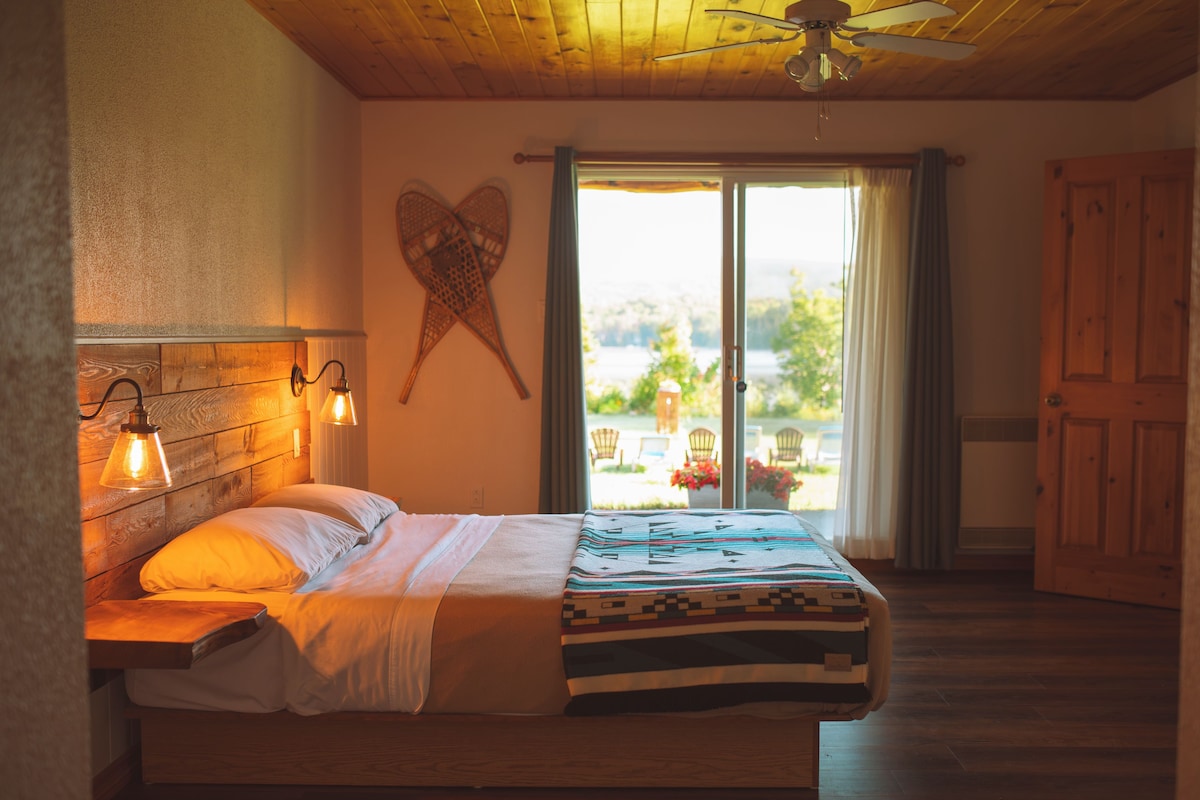 A bedroom with a bed, a ceiling fan, a wall-mounted light fixture, and a view through a sliding glass door.