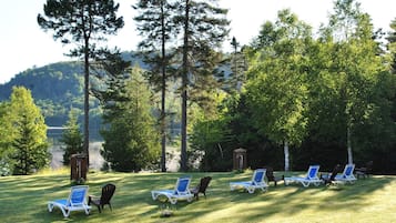 Une zone herbeuse où des chaises longues sont disposées en rangées, entourée d’arbres, avec une vue sur un lac et des collines en arrière-plan.