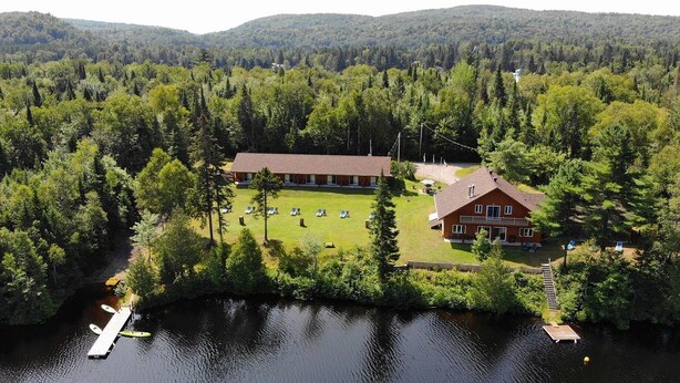 A lodge with a large deck area, a dock, and a forested backdrop. - L'Ours Bleu (Lac-Saguay)