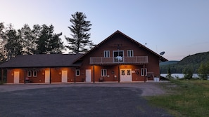 A two-story lodge with a balcony, a reception desk, and a view of the surrounding forest. - L'Ours Bleu (Lac-Saguay)