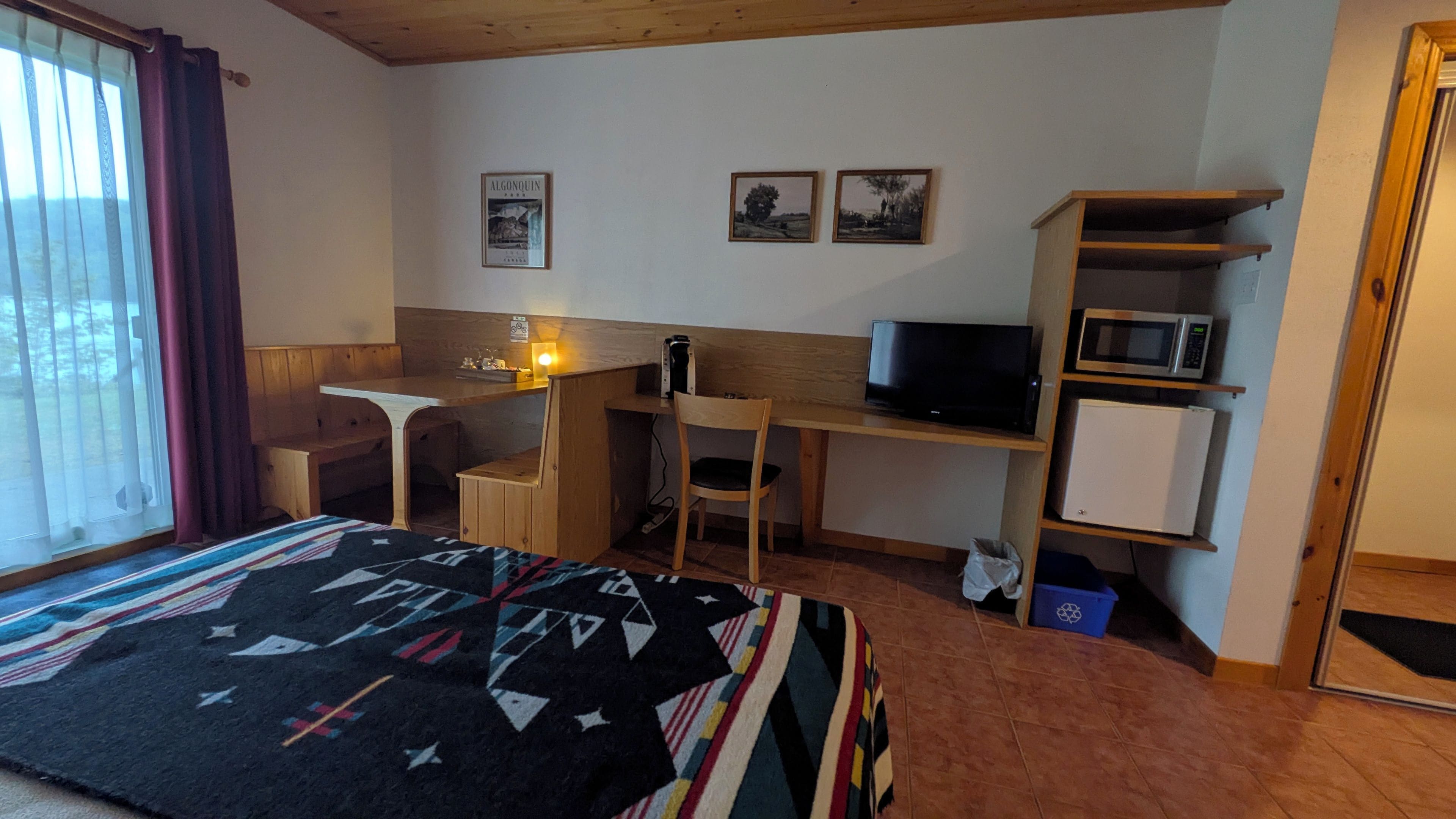 A hotel room with a bed, desk, chair, television, microwave, and a small refrigerator.