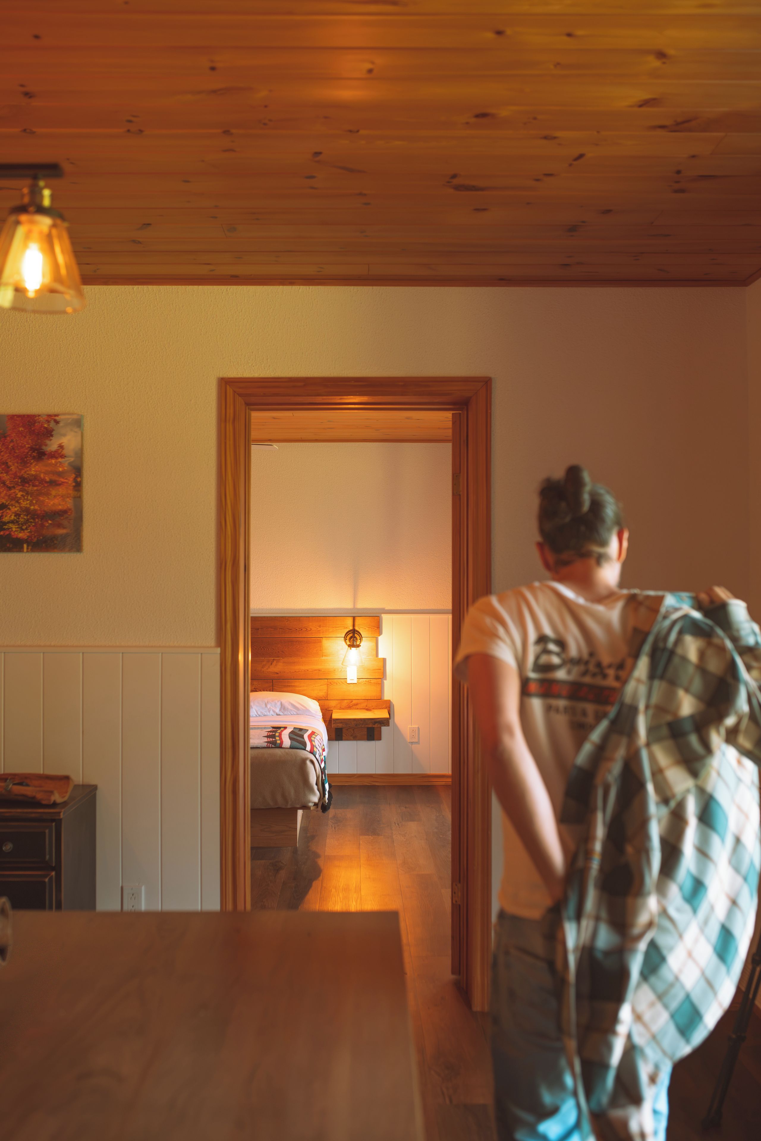 Une pièce avec un plafond en bois, un lit doté d’une tête de lit blanche, une table de chevet et une lampe fixée au mur.