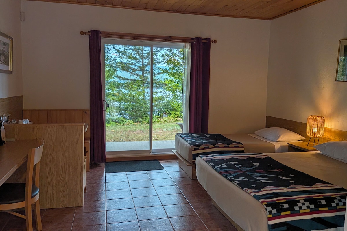 A hotel room with a desk, two beds, a chair, and a view of the outdoors.