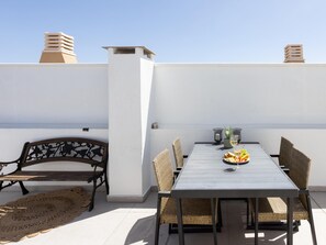Eine Dachterrasse mit Esstisch, Stühlen, einer Bank und Blick aufs Meer.