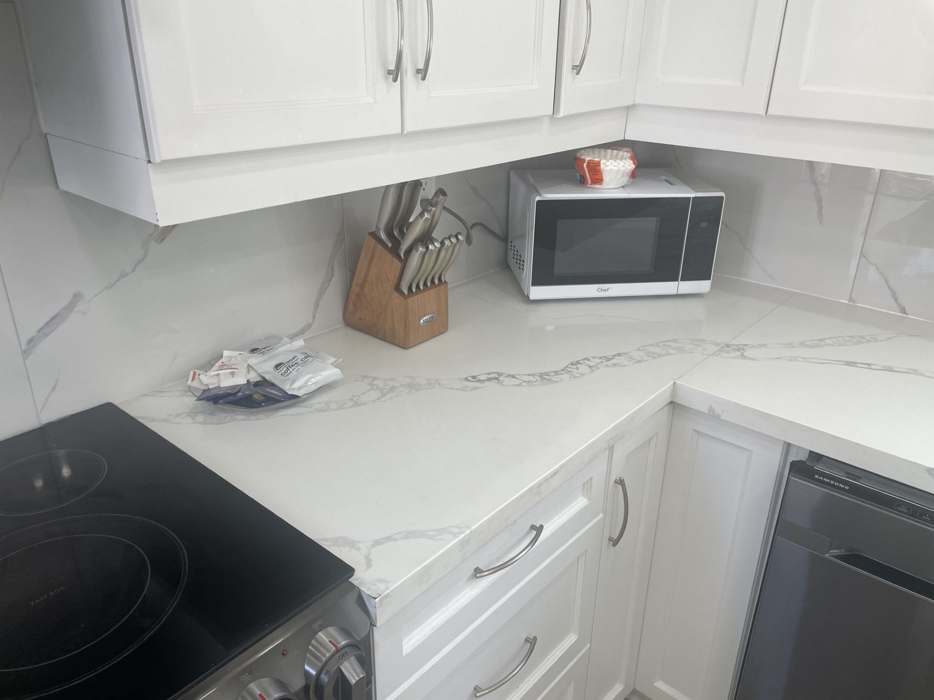 A kitchen with white cabinets, a microwave, a knife block, and a dishwasher.