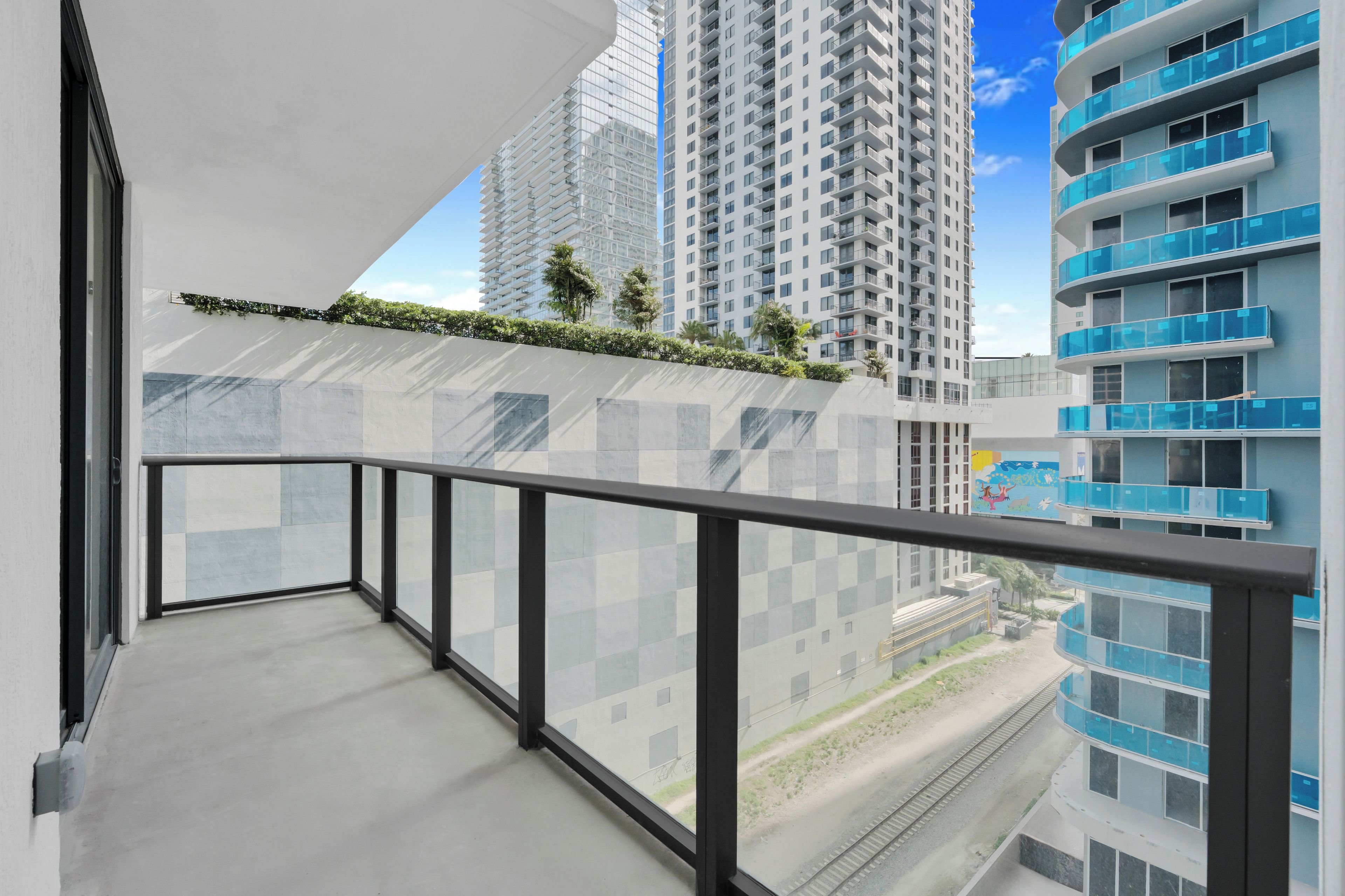 A balcony with a view of high-rise buildings and a railway track.
