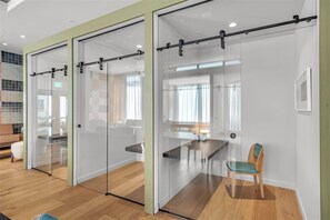 A modern office space with glass partitions, a wooden floor, a dining table, and a single chair. - The Crosby by Ilios Rentals (Miami)