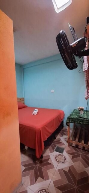 Una habitación con cama, una mesita con mantel verde y un ventilador de techo.
