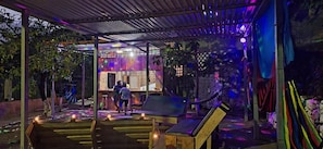 An outdoor area with a covered seating area, a stage, and a pool.