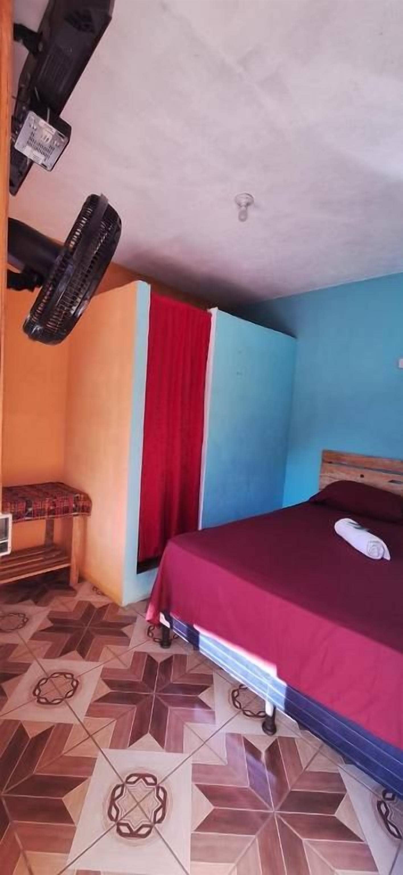 Una camera da letto con un letto, un comodino, una tenda rossa e un pavimento decorato.