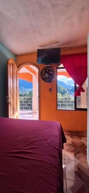 Una habitación con cama, ventilador, televisión y ventana con vistas.