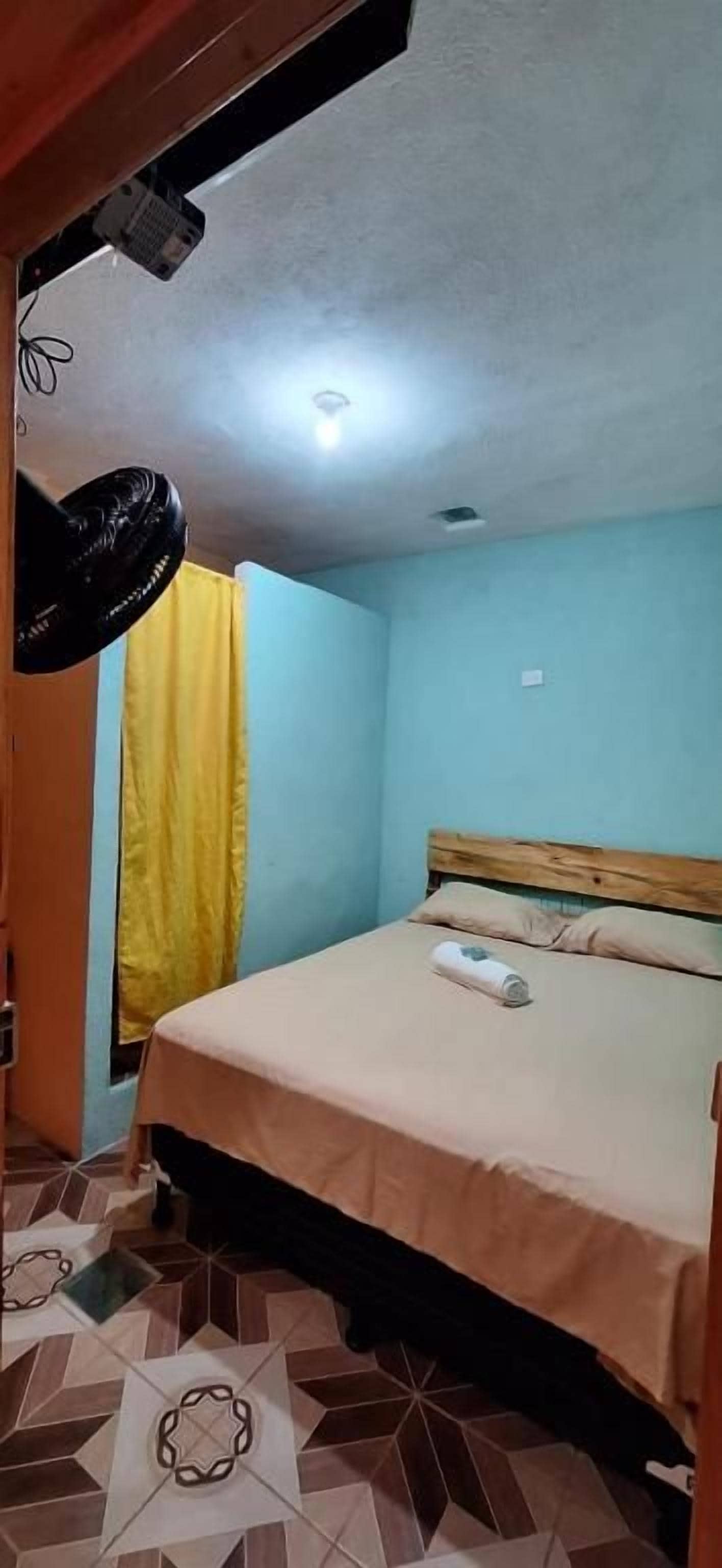 Quarto com cama, ventilador e janela com cortinas.